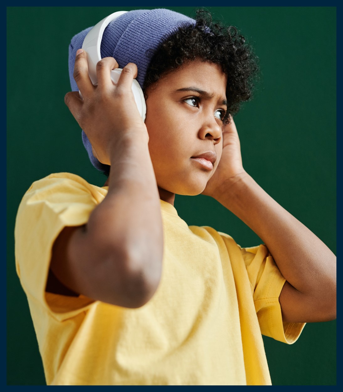 Boy in a beanie with hands over his headphones.