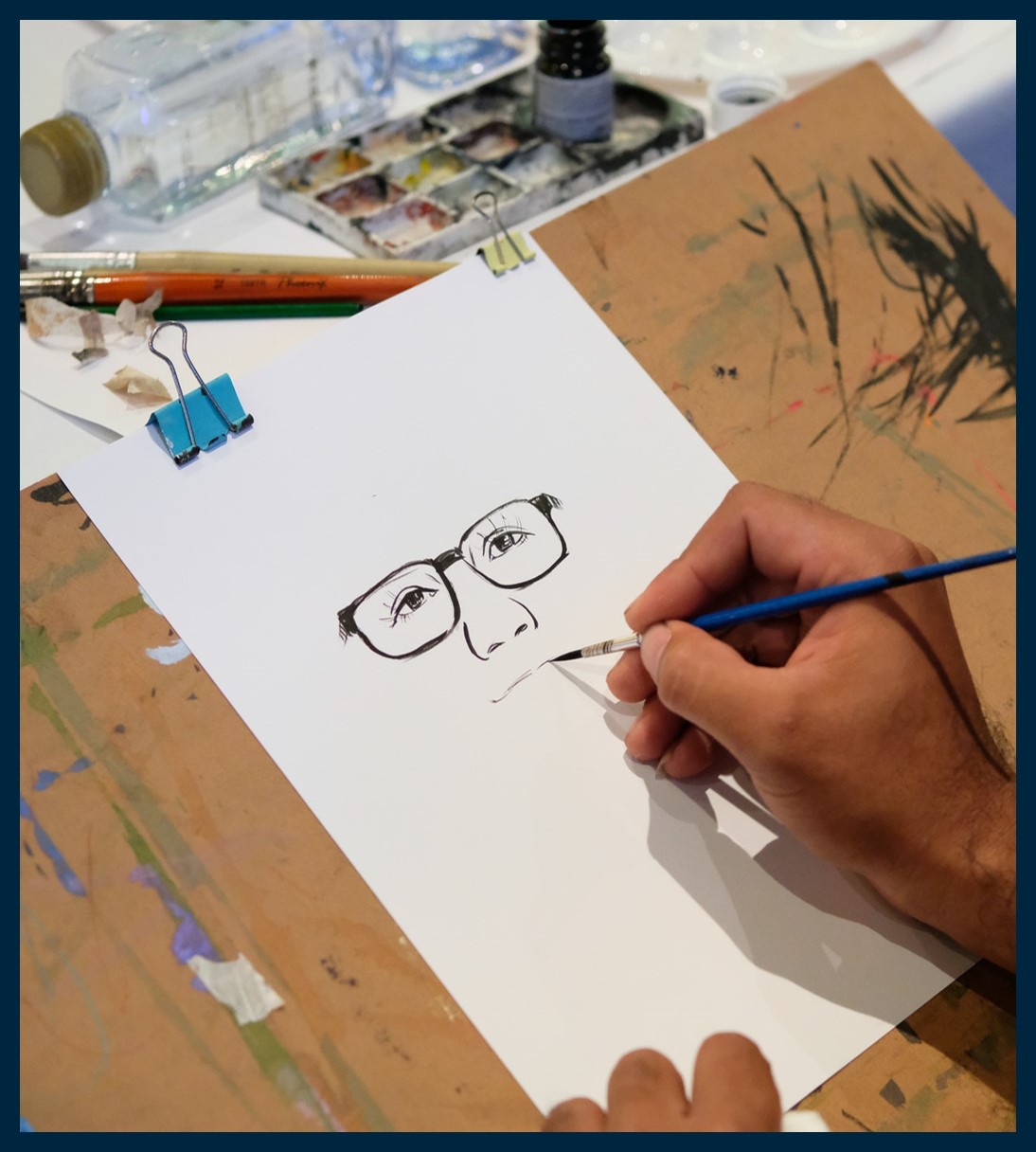 Person painting with ink. The picture is a face with glasses.